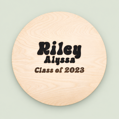 Round wooden graduation guest book personalized Riley Alyssa, Class of 2023, on a soft sage background.