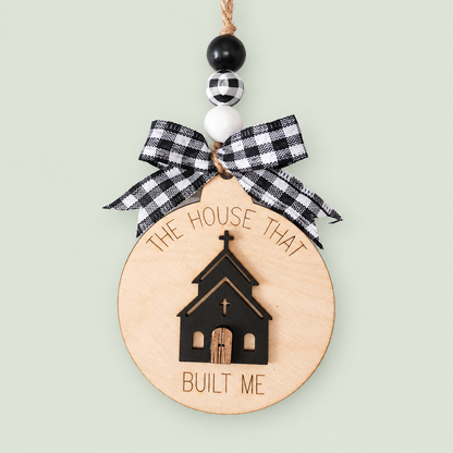 Layered wood church ornament reading The House That Built Me, with a black-and-white checked bow and beads.
