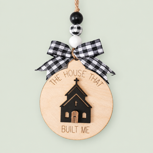 Layered wood church ornament reading The House That Built Me, with a black-and-white checked bow and beads.