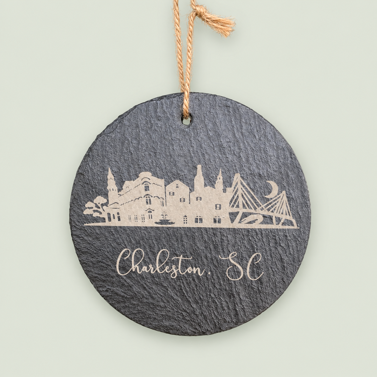 Round gray slate ornament engraved with the Charleston skyline and Charleston, SC.
