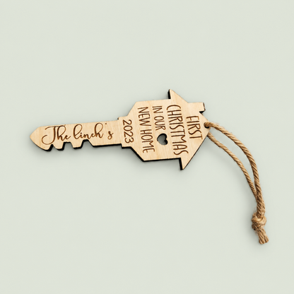 Personalized wooden house-key ornament engraved First Christmas in Our New Home, with a jute loop.
