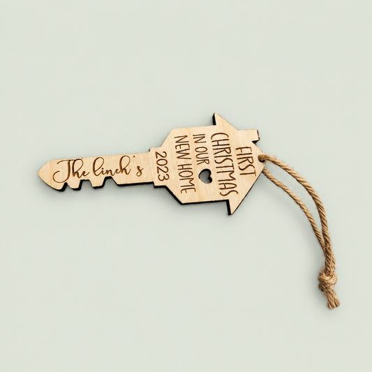 Personalized wooden house-key ornament engraved First Christmas in Our New Home, with a jute loop.