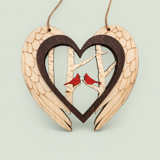 Wooden angel-wing heart ornament with two red cardinals perched among birch trees.