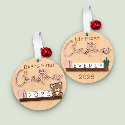 Two wooden baby's first Christmas ornaments with pink lettering, miniature shelf decorations and white ribbons on soft sage.