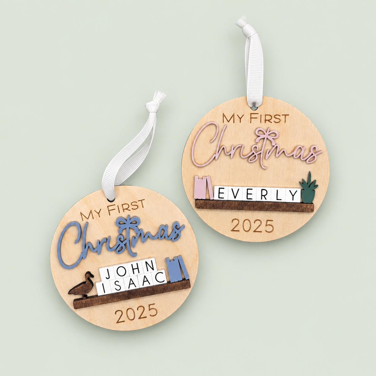 Personalized wooden first Christmas ornaments for John Isaac and Everly with blue and pink lettering on soft sage.