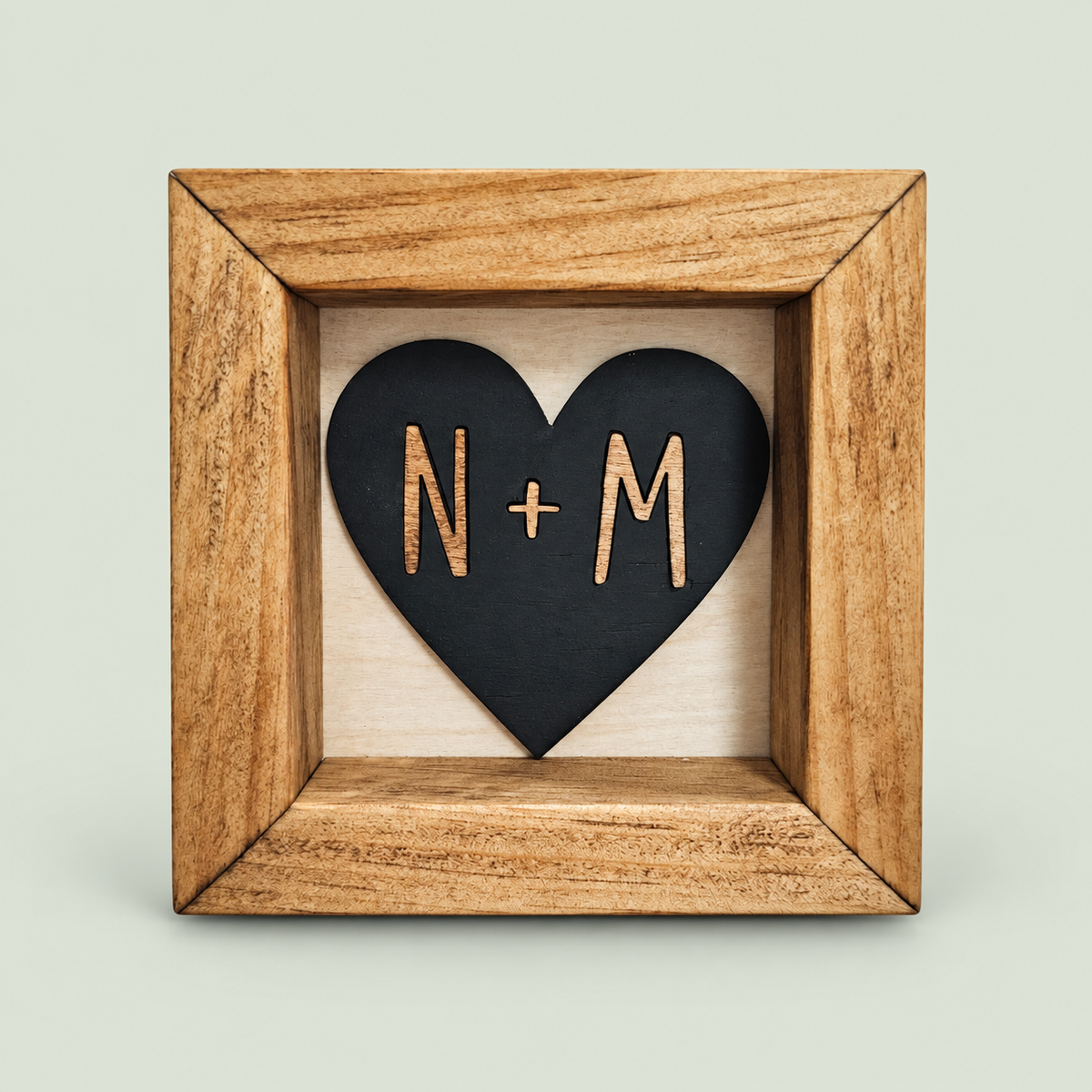 Wood-framed black heart sign with personalized N and M initials on a soft sage background.