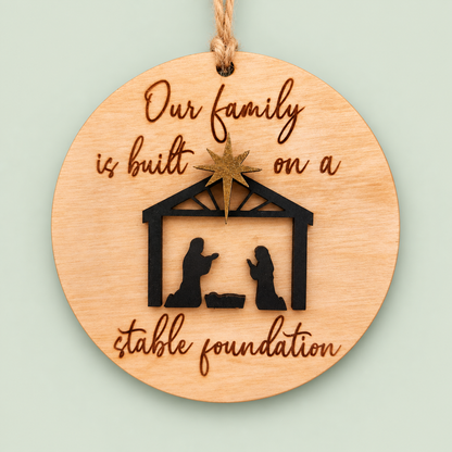 Round wooden stable foundation ornament with a black nativity scene and gold star on soft sage.