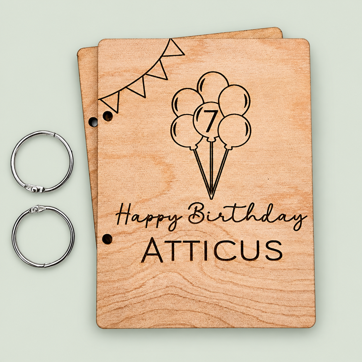 Personalized wooden birthday card keeper for Atticus with balloons, age seven and two binder rings on soft sage.