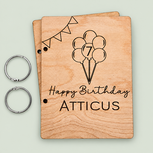 Personalized wooden birthday card keeper for Atticus with balloons, age seven and two binder rings on soft sage.