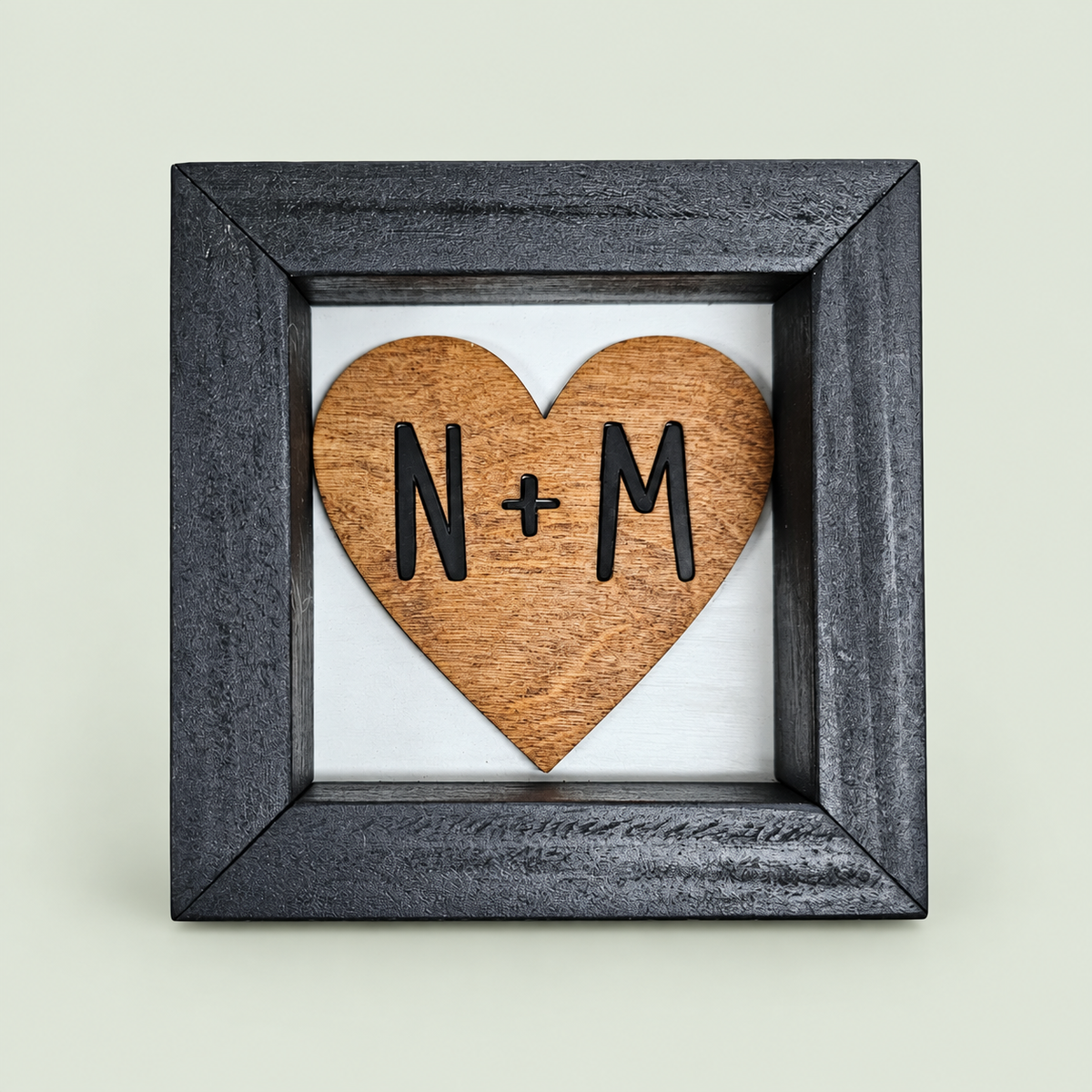 Black-framed wooden heart sign with personalized N and M initials on soft sage.