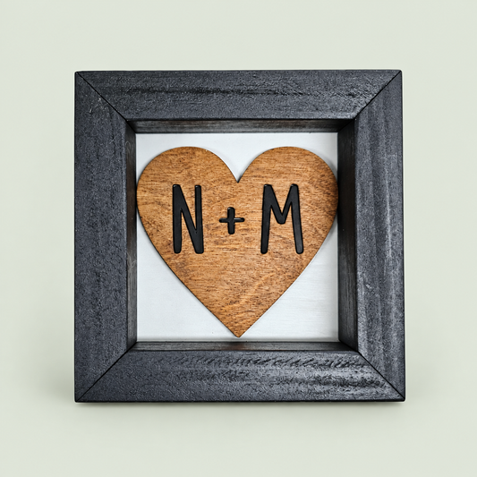 Black-framed wooden heart sign with personalized N and M initials on soft sage.