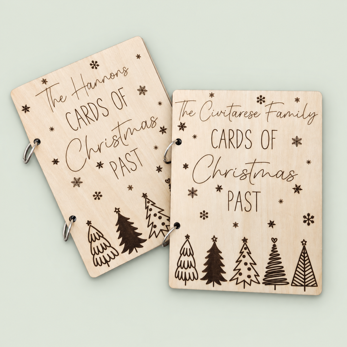 Two personalized wooden Christmas card keepers with engraved trees and snowflakes on a soft sage background.