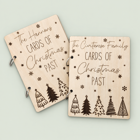 Two personalized wooden Christmas card keepers with engraved trees and snowflakes on a soft sage background.