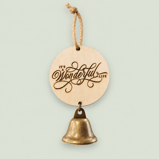 Round wooden It's a Wonderful Life ornament with an antique-style gold bell on soft sage.