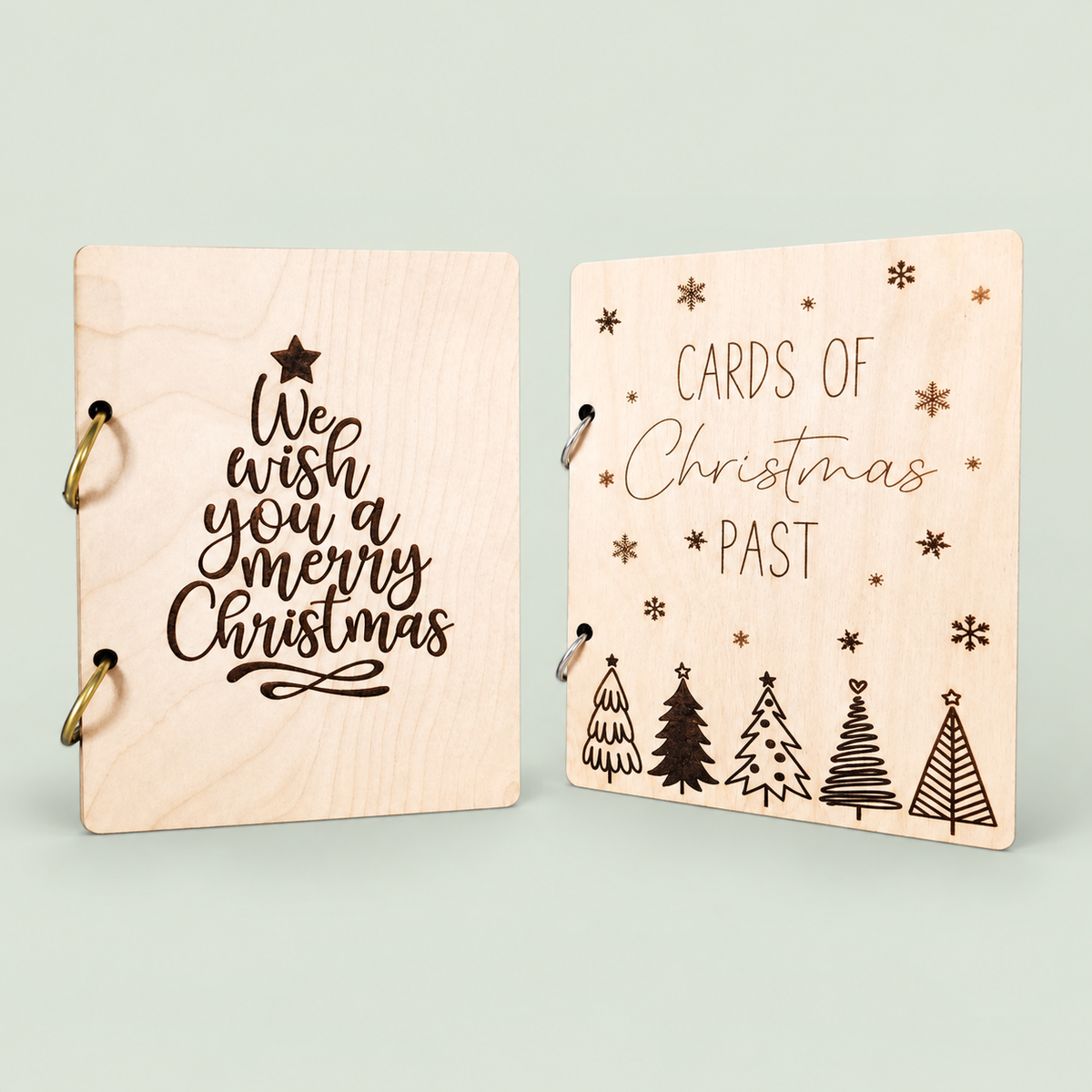 Two wooden Christmas card keepers with holiday lettering, engraved trees and binder rings on soft sage.