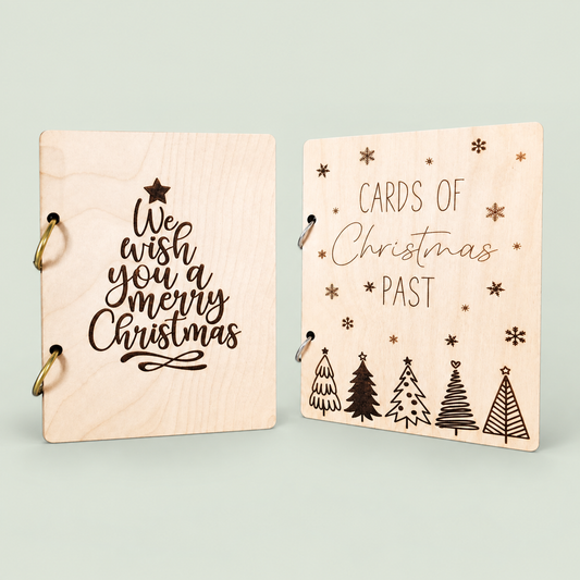 Two wooden Christmas card keepers with holiday lettering, engraved trees and binder rings on soft sage.