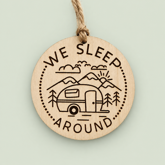 Round wooden We Sleep Around camper ornament with mountains and a twine hanger on soft sage.